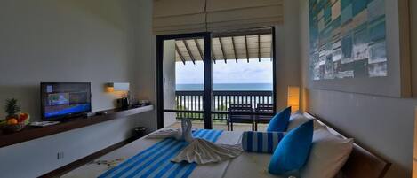 Habitación de hotel con cama, televisión, balcón con vistas y un cuadro en la pared.