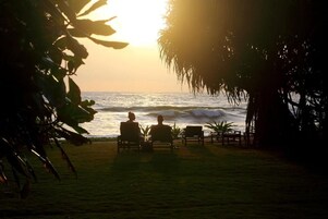 Dos personas sentadas en sillas frente al océano al atardecer.