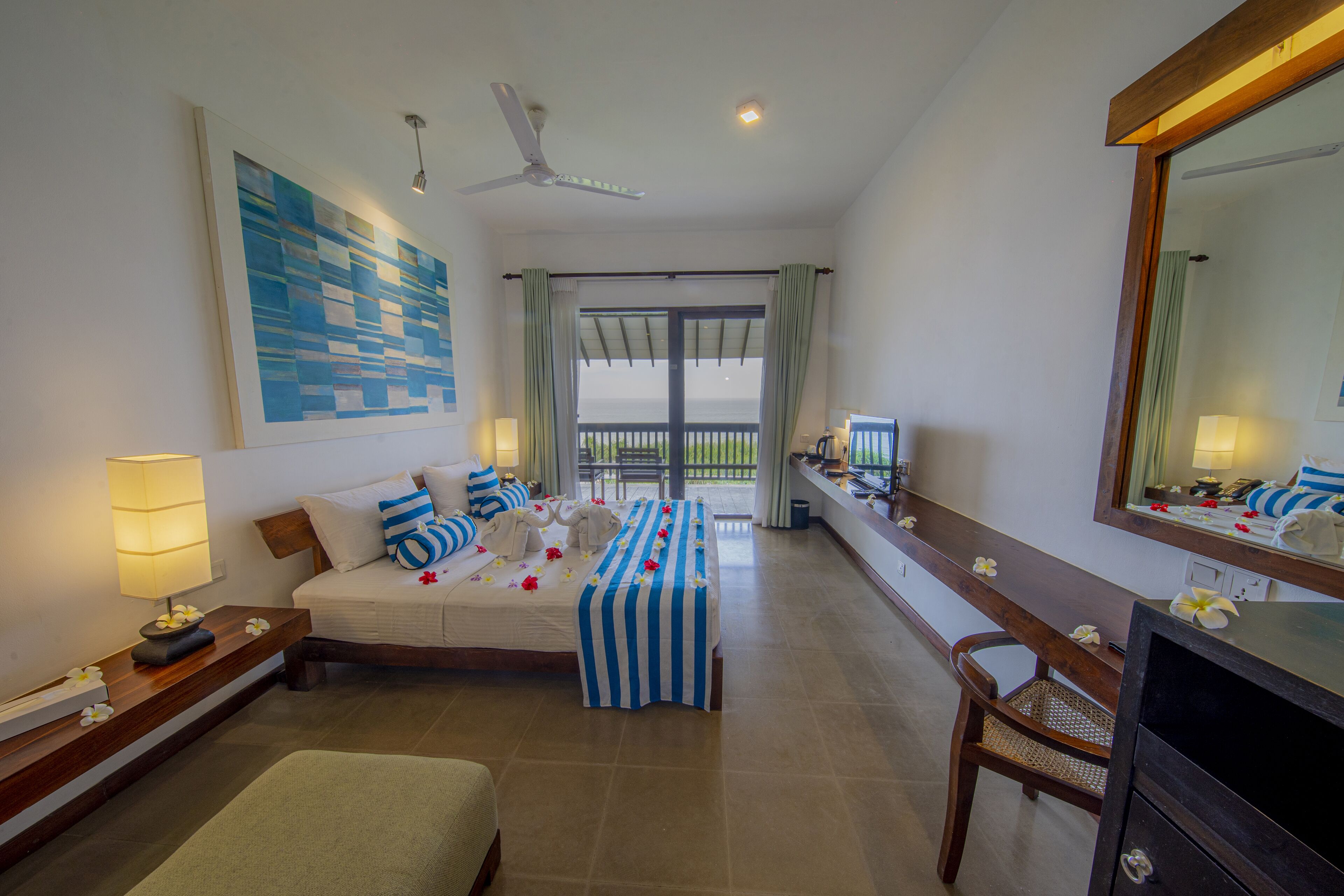 A hotel room with a bed, a desk, a chair, a large mirror, and a balcony with a view.