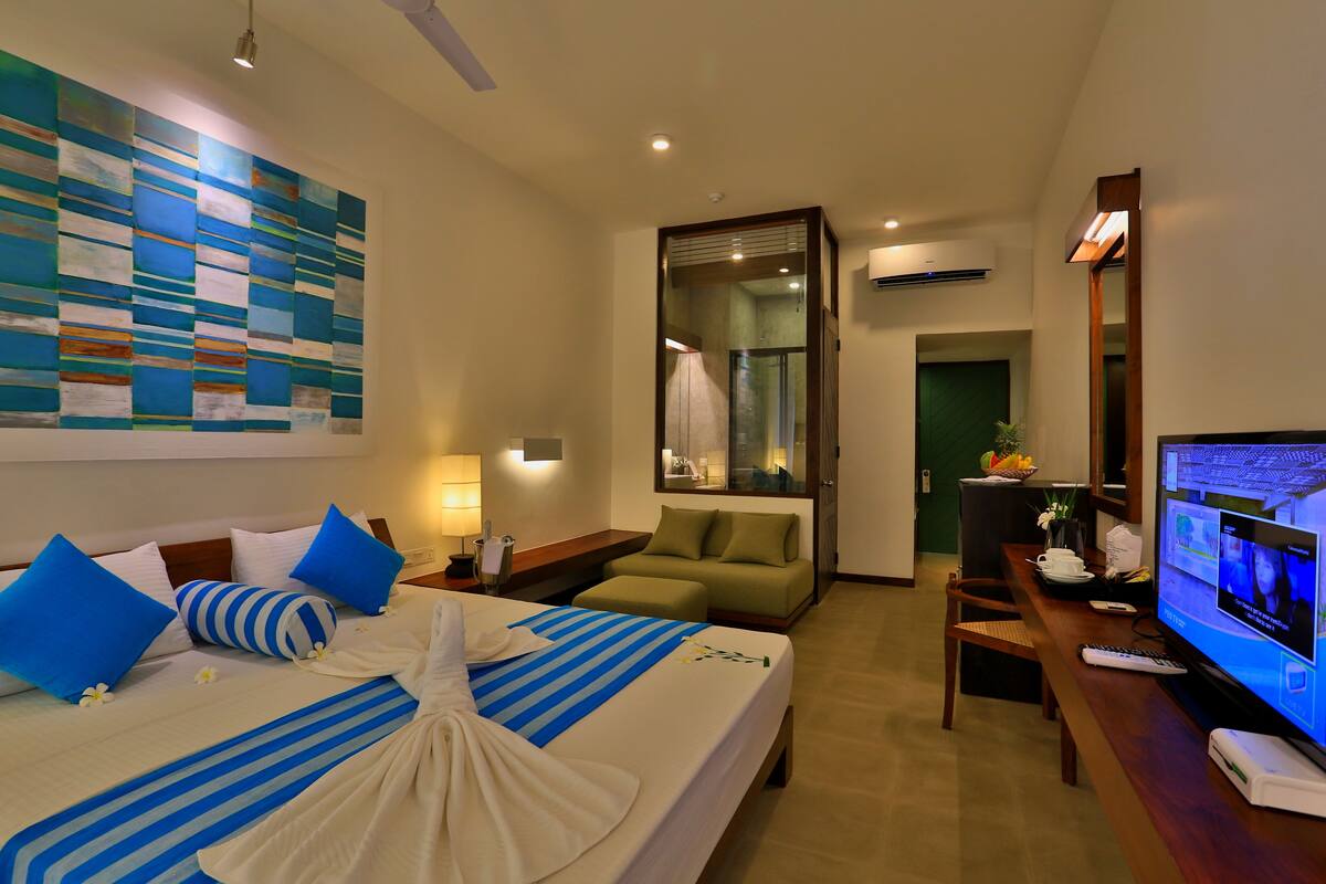 A hotel room with a large bed, a television, a desk, and a seating area.