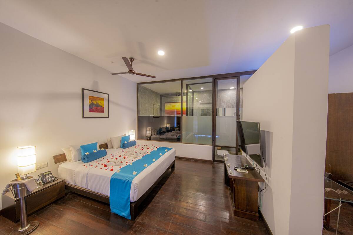 A modern hotel room with a large bed, bedside table, desk, and a television.
