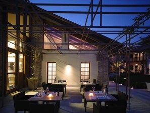 An outdoor dining area with tables and chairs, a brick wall, and a wooden pergola structure. - Hotel Mulino Grande (Cusago)