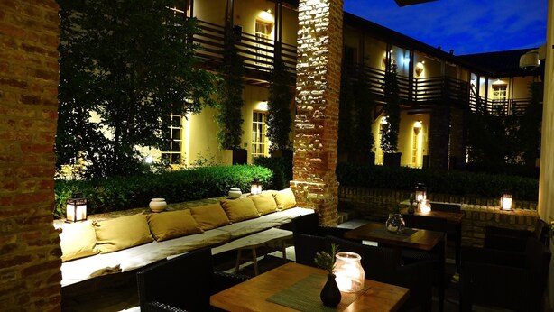 An outdoor seating area with a bench, tables, and lanterns, surrounded by greenery and a brick wall. - Hotel Mulino Grande (Cusago)