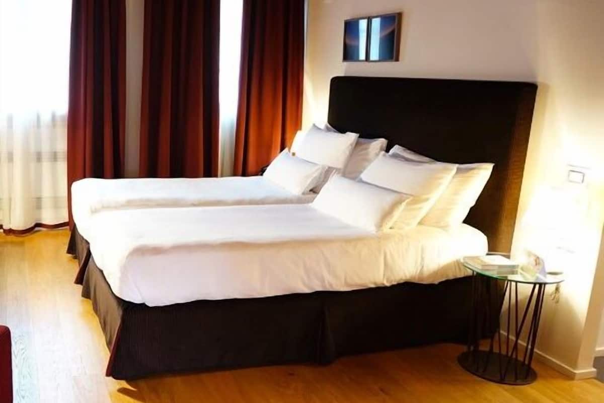 A double bed with white linens, a dark headboard, and a bedside table with a lamp.
