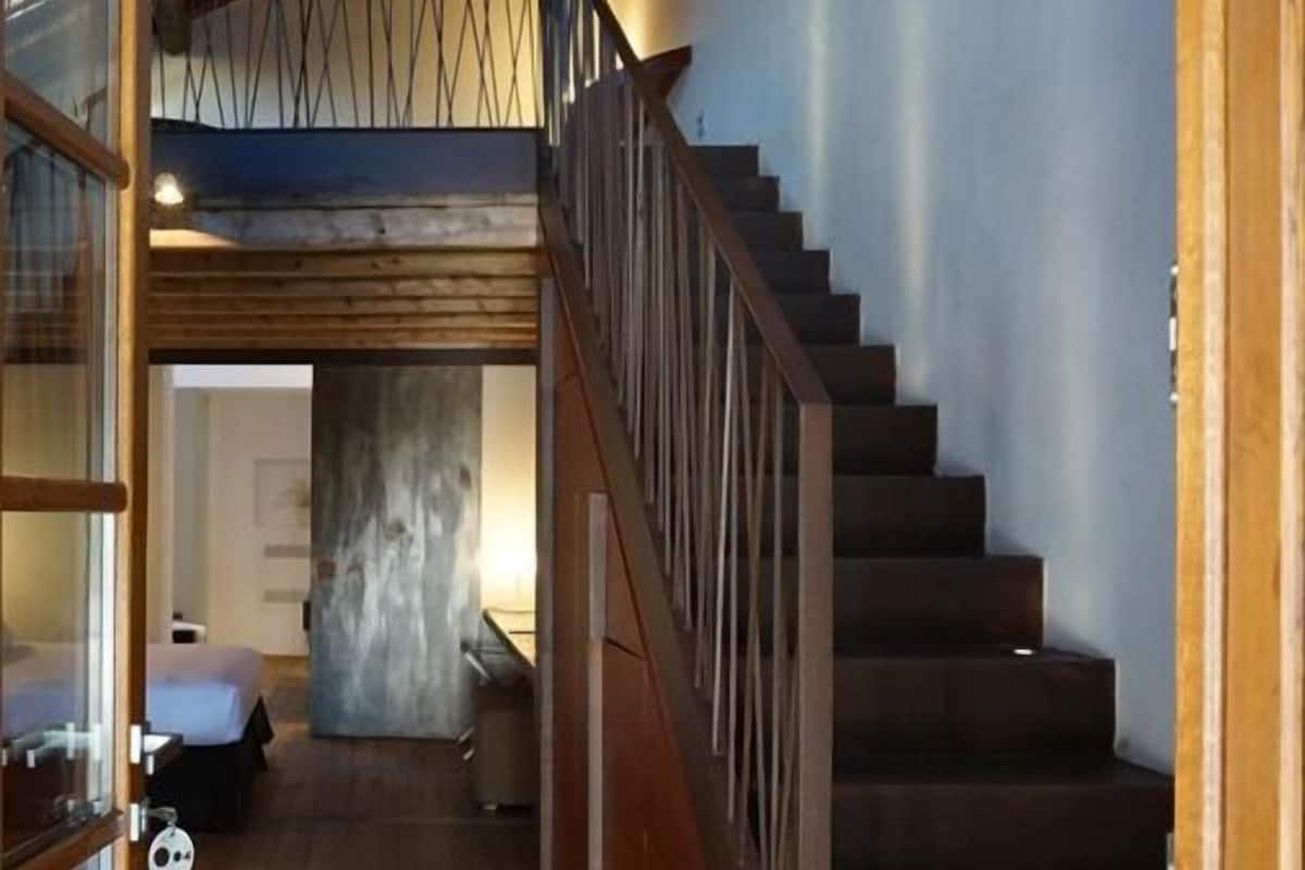 A wooden staircase leading to a second floor, with a view of a room with a bed and a small table.