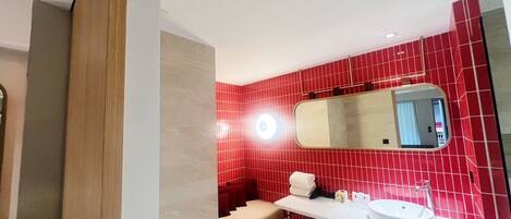 A modern bathroom with red tiled walls, a white sink, and a mirror above it.