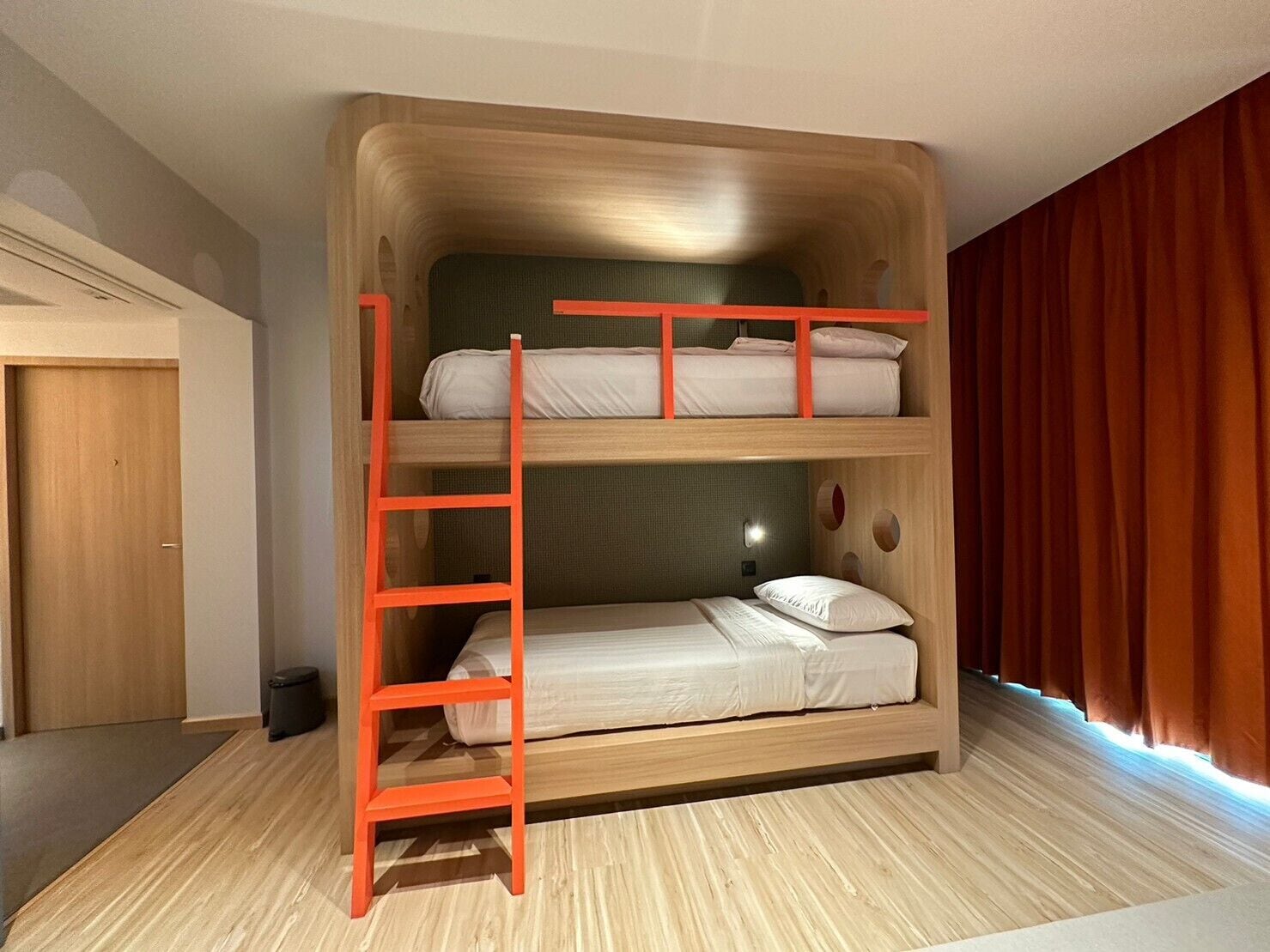 A bunk bed room with a wooden ladder, a door, and a curtain.