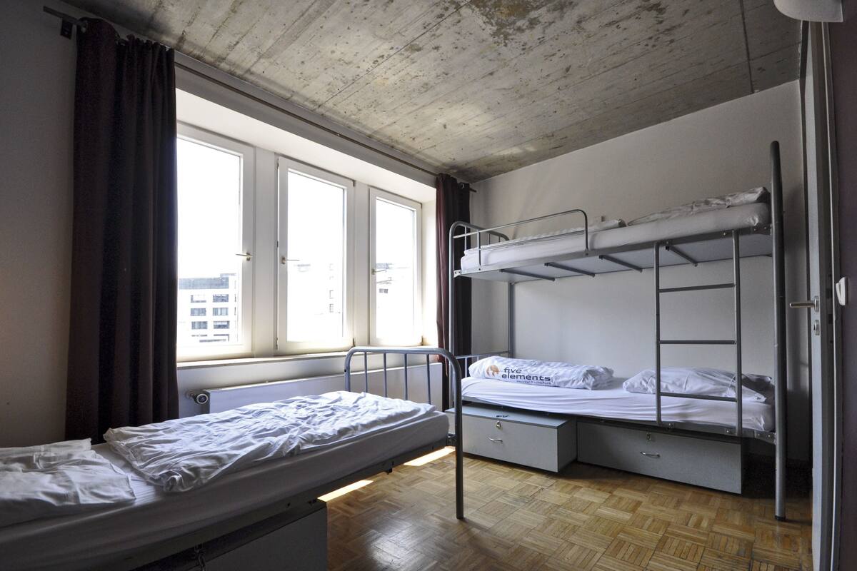 A dormitory room with two bunk beds, a window with curtains, and a radiator.