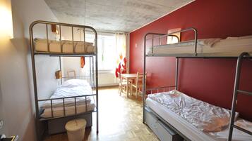 Un dormitorio con literas, suelo de madera, una mesa y una silla.
