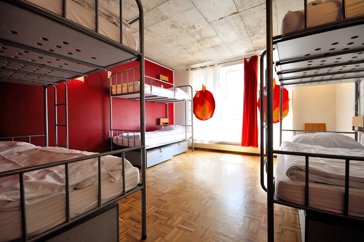 A dormitory room with bunk beds, a wooden floor, and a red wall.