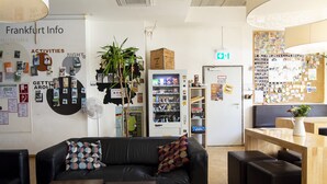 A modern lobby with a black leather couch, a vending machine, and a bulletin board with various notices. - Five Elements Hostel (Frankfurt)