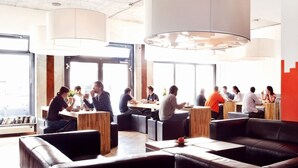 A modern cafe with leather seating, large windows, and hanging light fixtures. - Five Elements Hostel (Frankfurt)