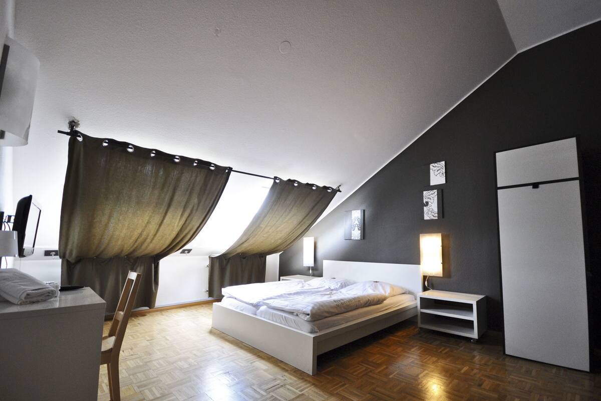 A modern bedroom with a large bed, a desk, and a wardrobe.