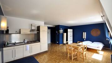 Una cocina compacta con armarios blancos, una mesa de comedor de madera y una cama con ropa de cama blanca.