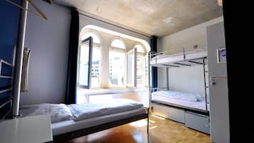 A dormitory room with bunk beds, a window with arched design, and a wooden floor.