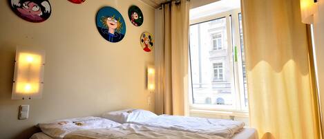 A hotel room with a bed, a window with curtains, and wall decorations.