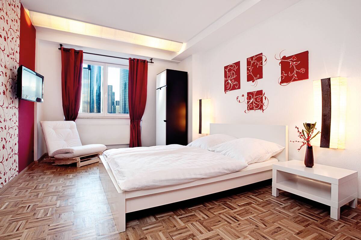 A modern bedroom with a bed, a bedside table, a chair, and a TV mounted on the wall.