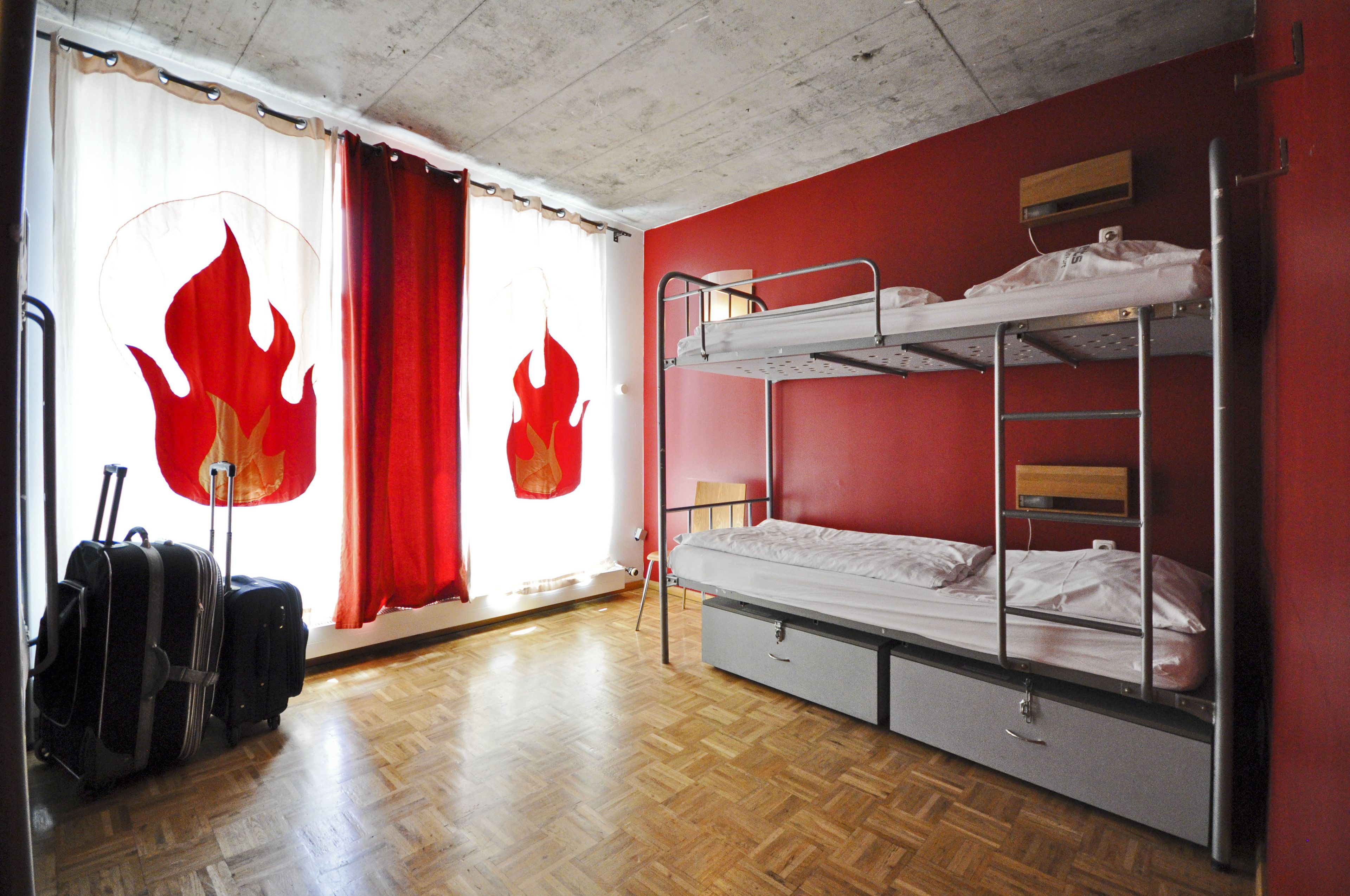 A room with a bunk bed, wooden flooring, and a window with curtains.