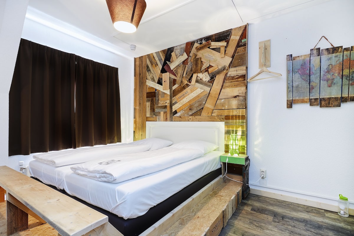 A bedroom with a wooden headboard, a bed with white linens, a wooden bench, and a wall-mounted map.