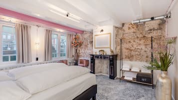 A bedroom with a large bed, a dresser, a vanity, and a brick wall.