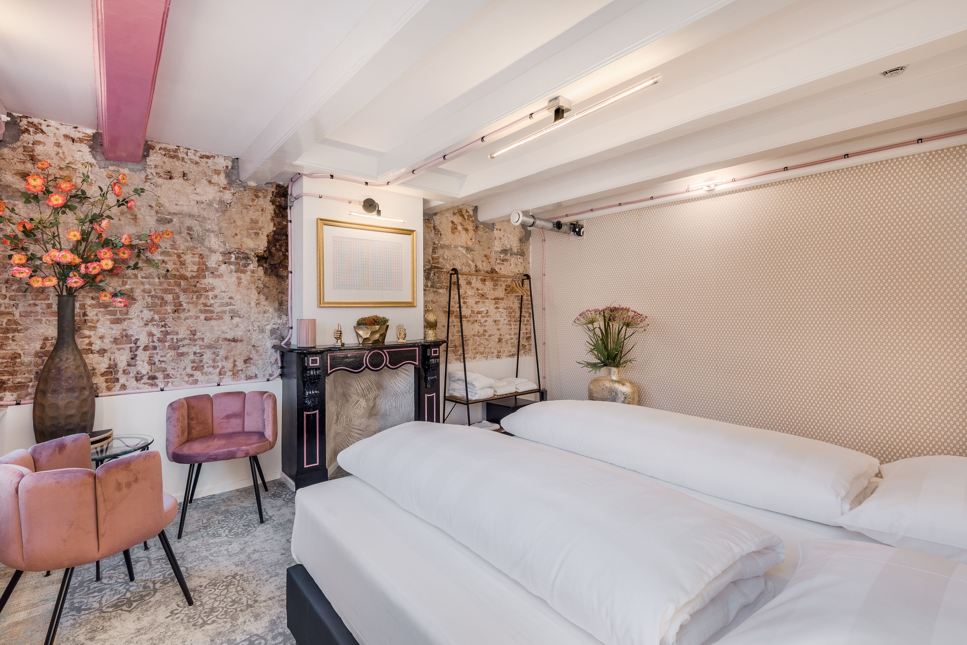 A modern bedroom with a brick wall, a large bed, a vanity with a mirror, and a pink chair.