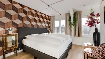 Un dormitorio moderno con una pared de estampado geométrico, una cama grande, un espejo, una silla y vistas de la ciudad a través de amplios ventanales.