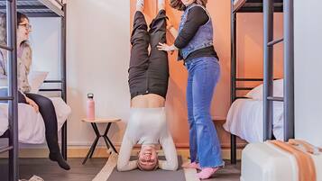 A dormitory room with bunk beds, a yoga mat, a small table with a pink water bottle, and a decorative wall piece.