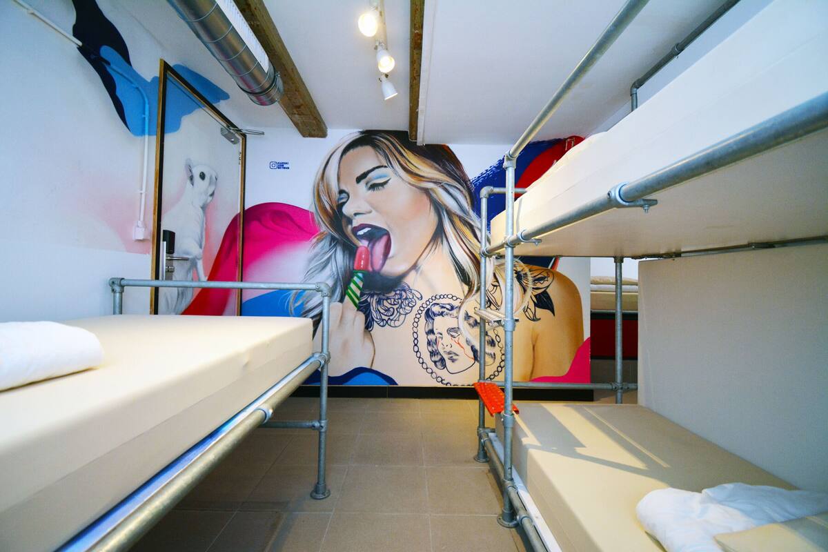 A dormitory room with bunk beds, a mural on the wall, and a visible electrical outlet.