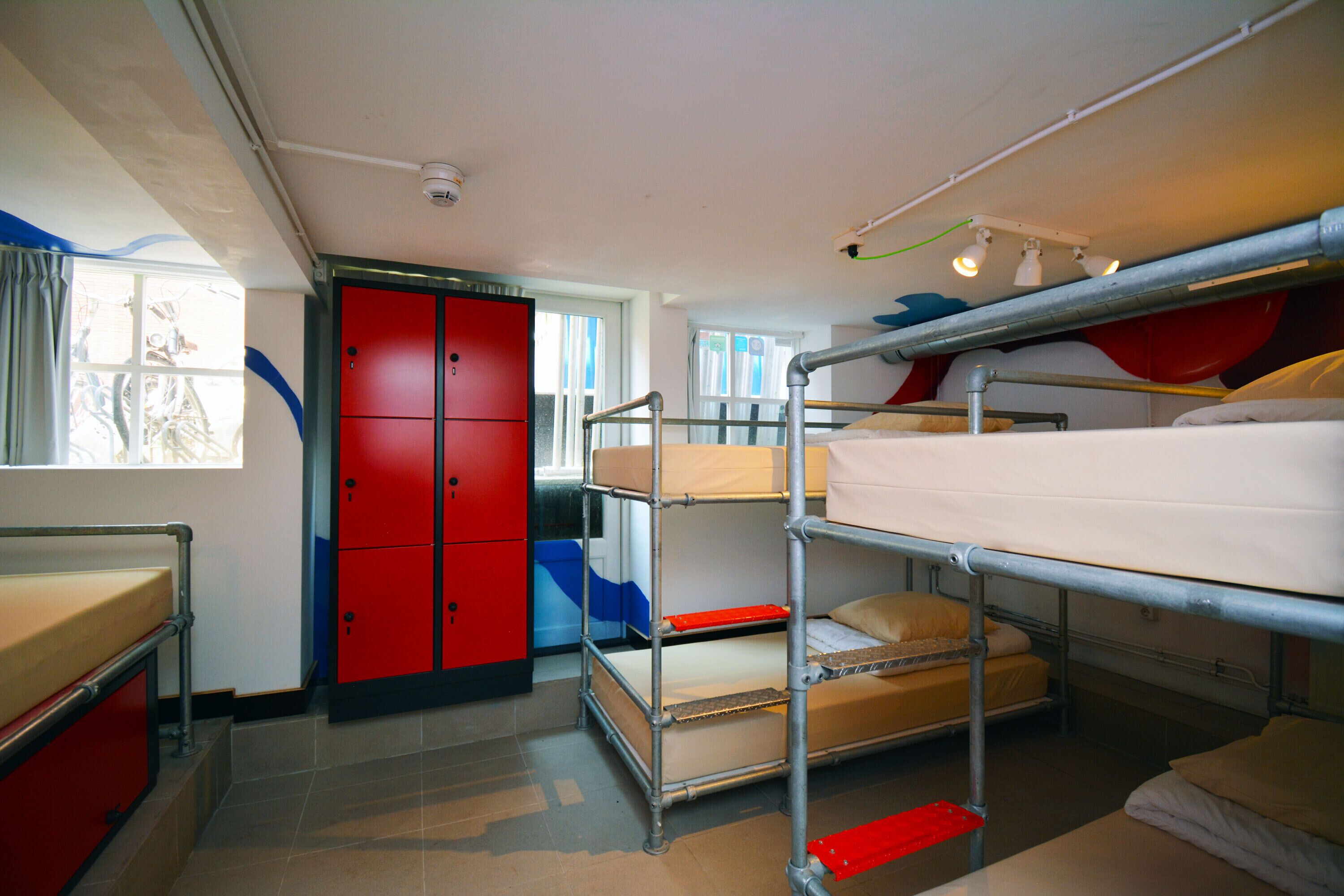 Un dormitorio con literas, un armario rojo y una ventana con cortinas.