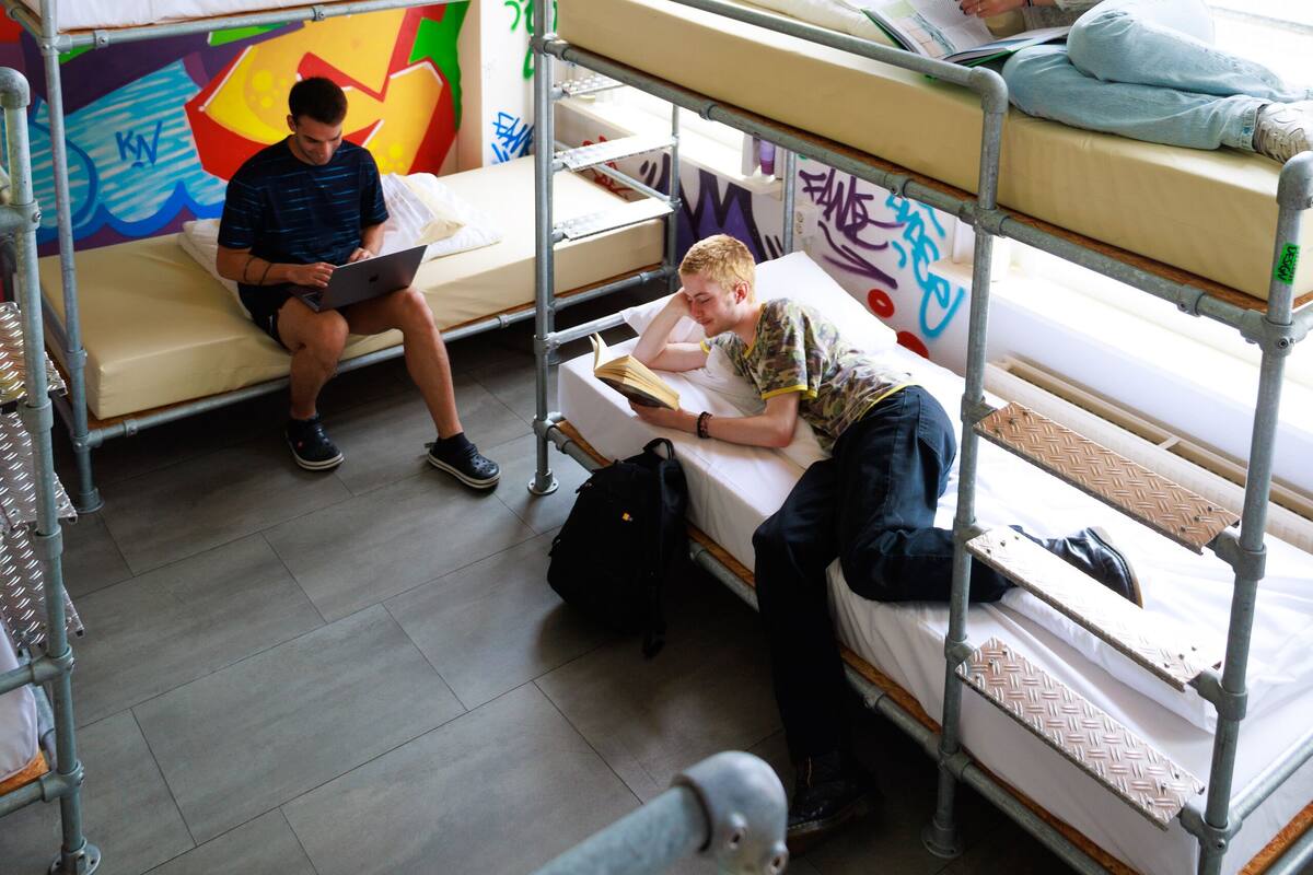 A dormitory room with bunk beds, graffiti on the walls, and a window with curtains.