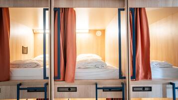 Une rangée de lits superposés avec des cadres en bois et des rideaux orange, chacun étant muni d’une petite étagère et d’un luminaire au-dessus.
