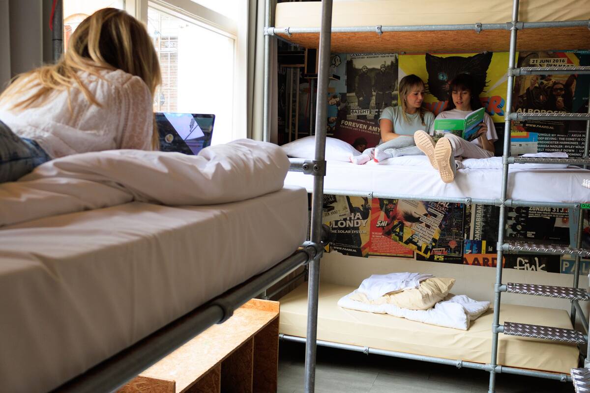 A bunk bed room with a laptop on the top bunk, a poster on the wall, and a window with blinds.