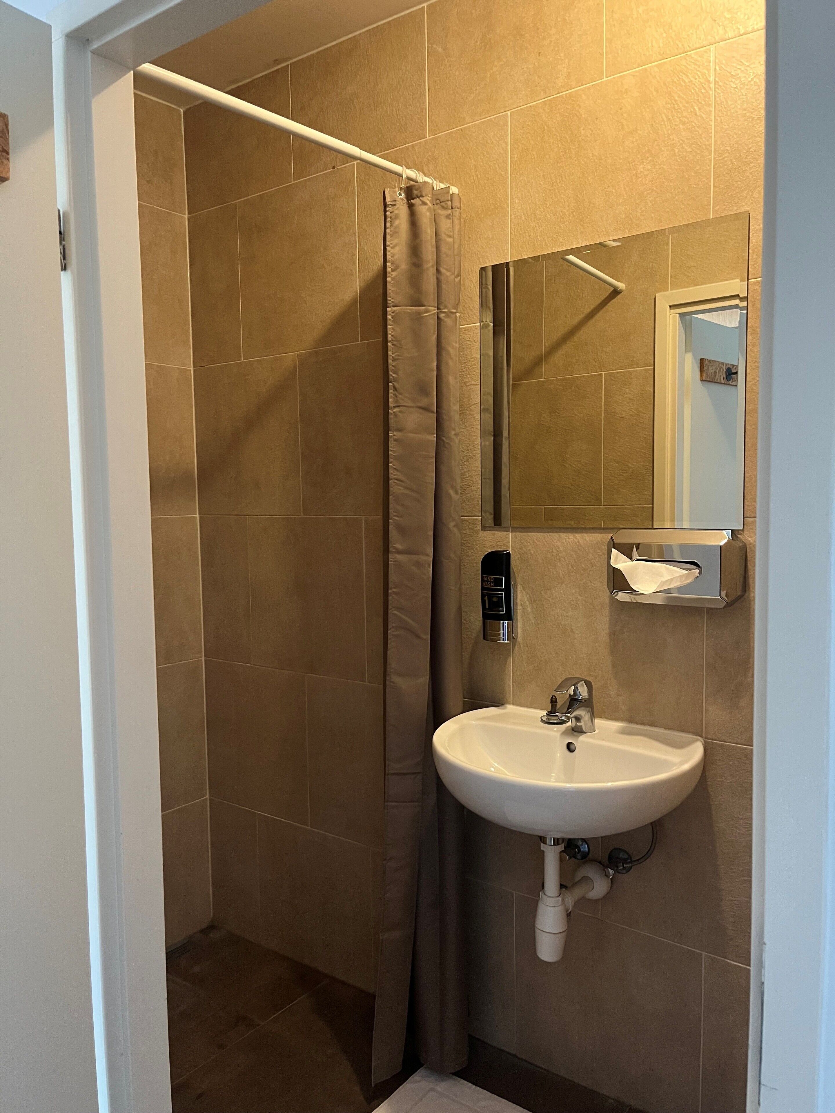 A bathroom with a shower, a sink, a mirror, and a towel dispenser.