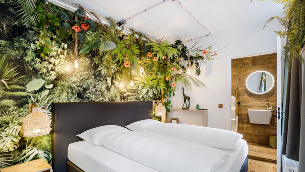 A bedroom with a bed, a wall-mounted mirror, a bedside table, and a wooden floor. - Will & Tate City Stay (The Hague)
