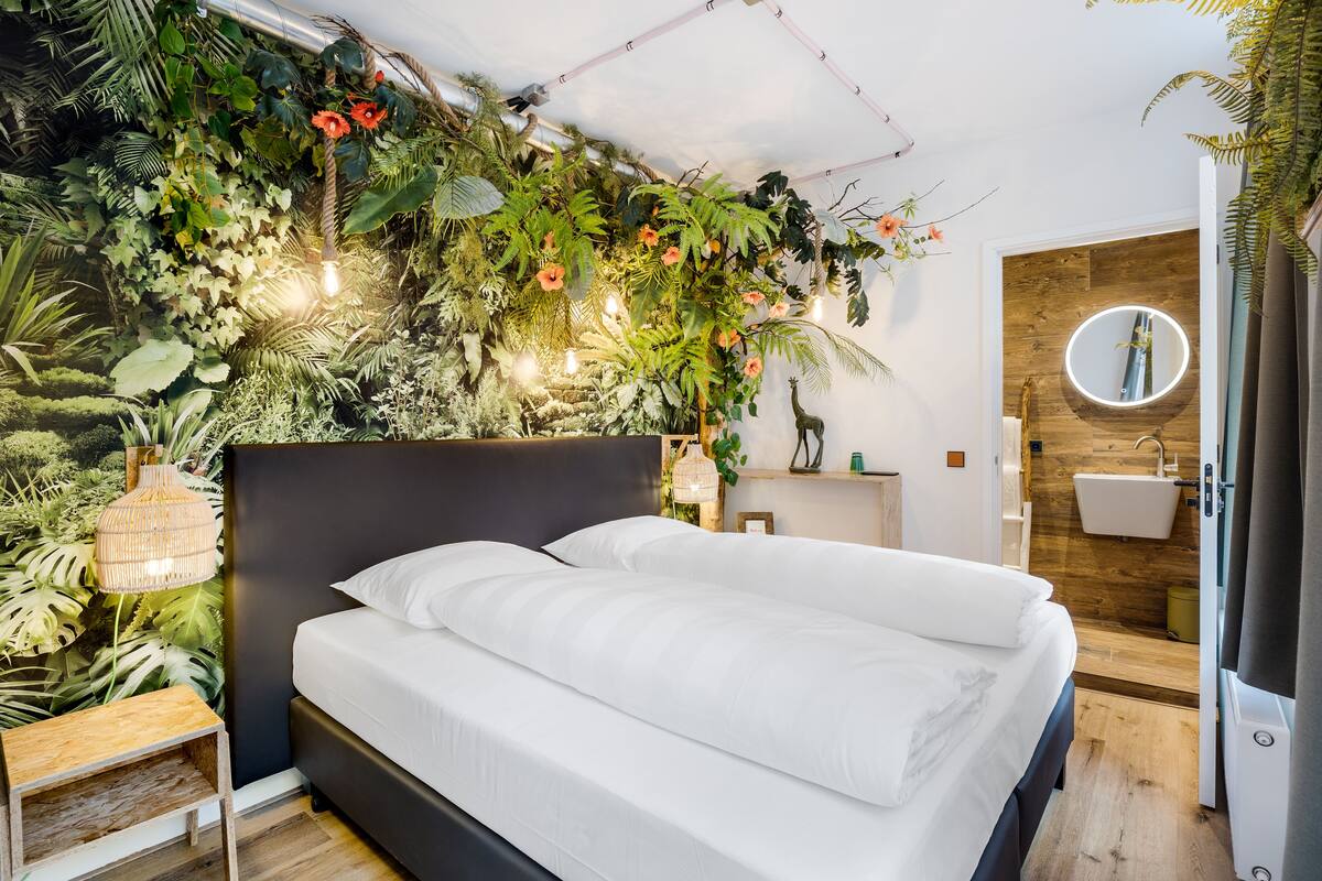 A bedroom with a bed, a wall-mounted mirror, a bedside table, and a wooden floor.