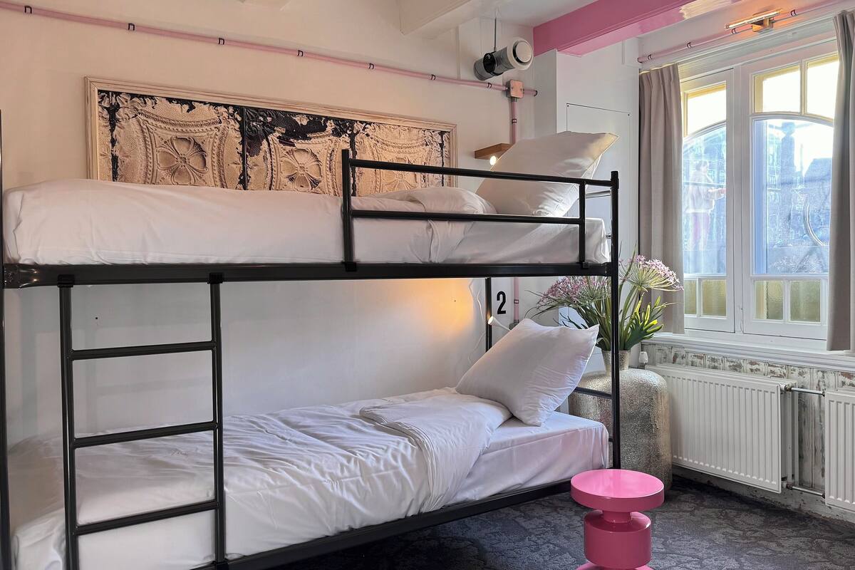 A bunk bed room with a window, a radiator, and a pink stool.