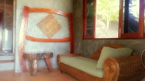 A wicker sofa with a cushion, a small wooden stool, and a decorative wall panel.