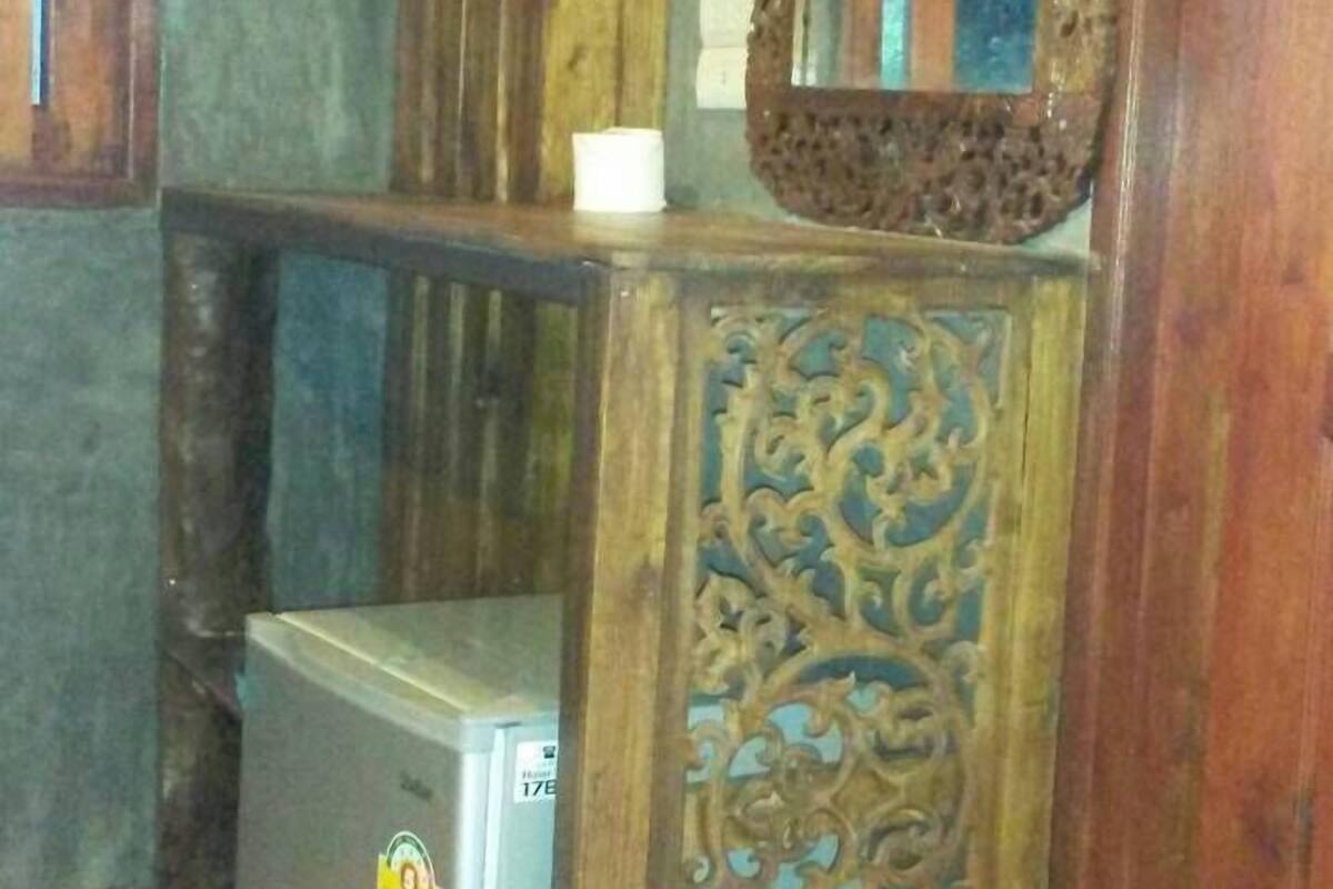 A corner of a room with a wooden cabinet, a small refrigerator, and a mirror on the wall.