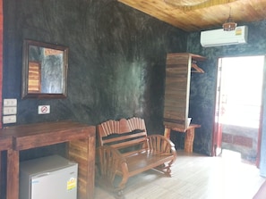 Una habitación con un banco de madera, un refrigerador pequeño, un espejo y un equipo de aire acondicionado.