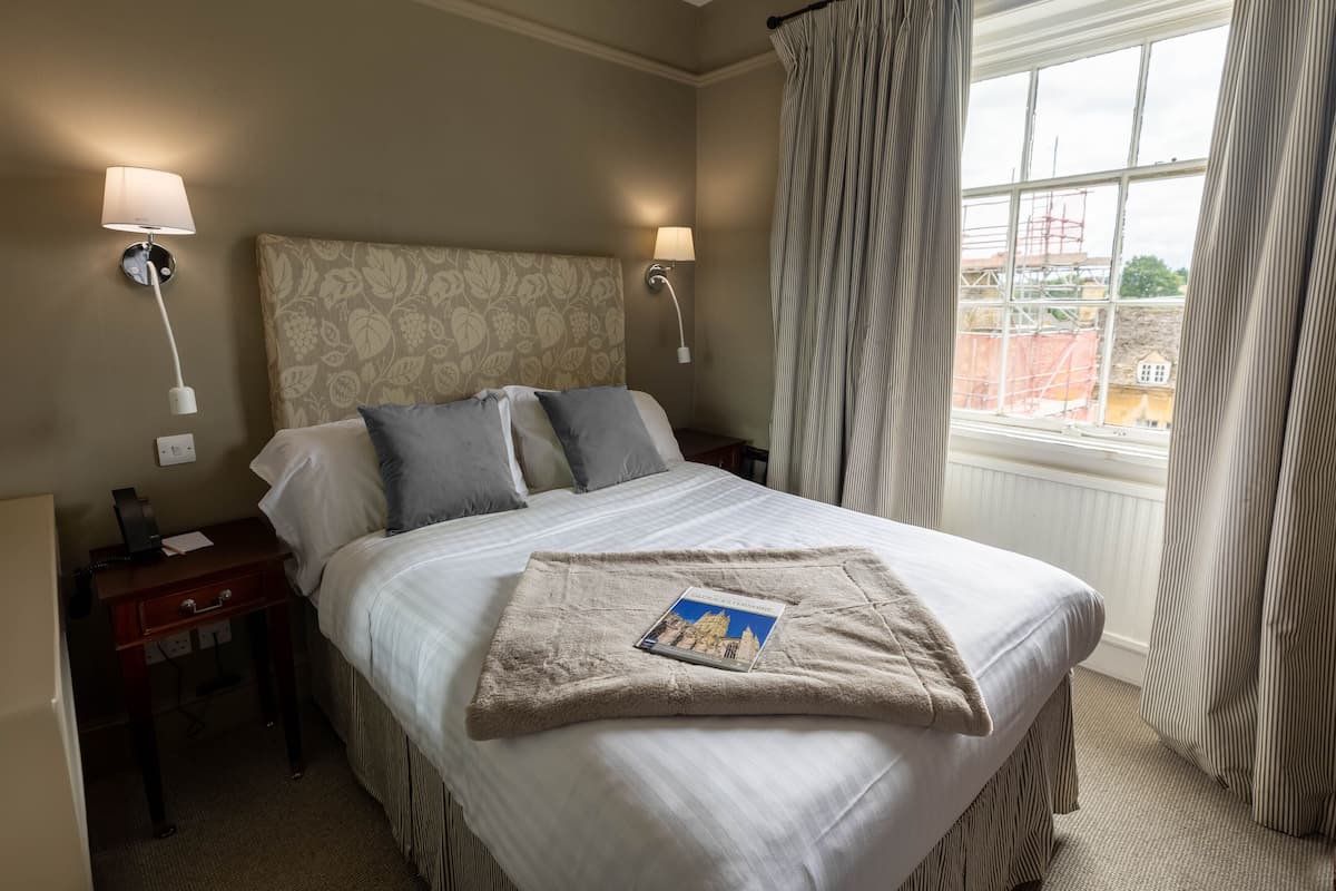 A hotel room with a large bed, two bedside lamps, a nightstand, and a window with curtains.