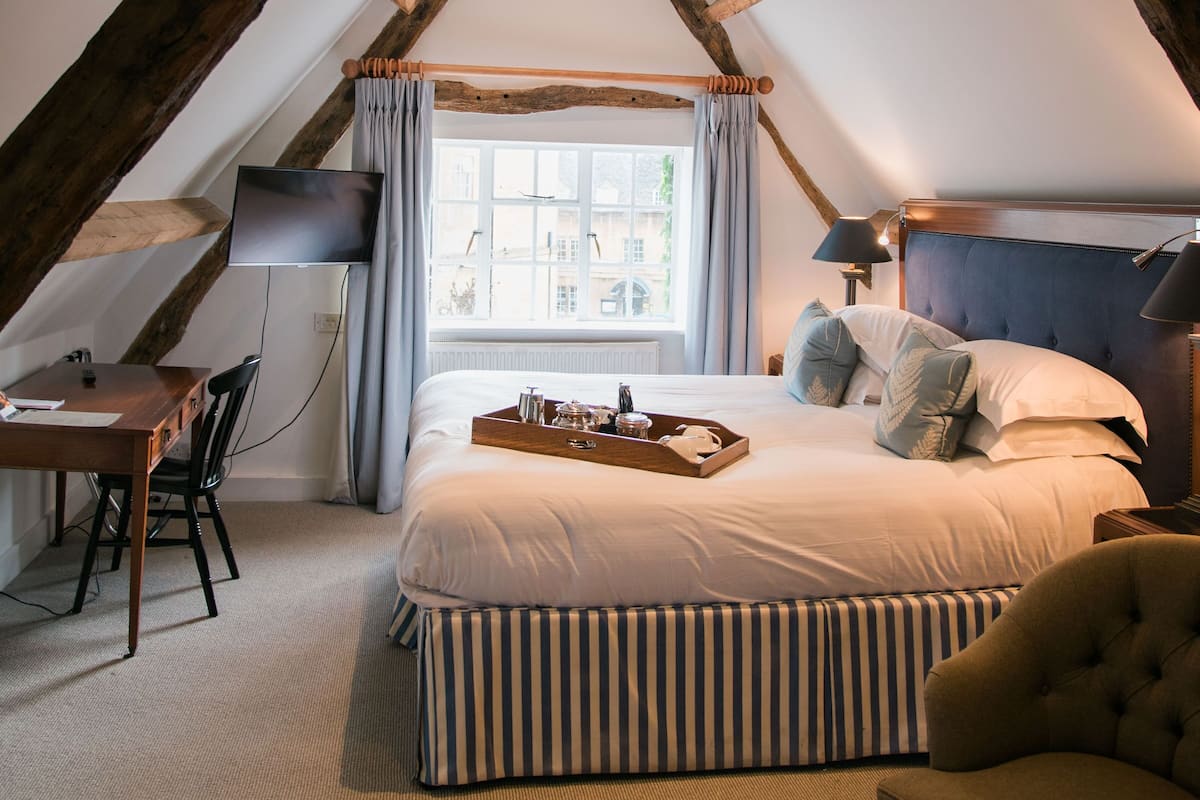 A bedroom with a sloped ceiling, a bed with striped bedding, a bedside table, a chair, and a television.