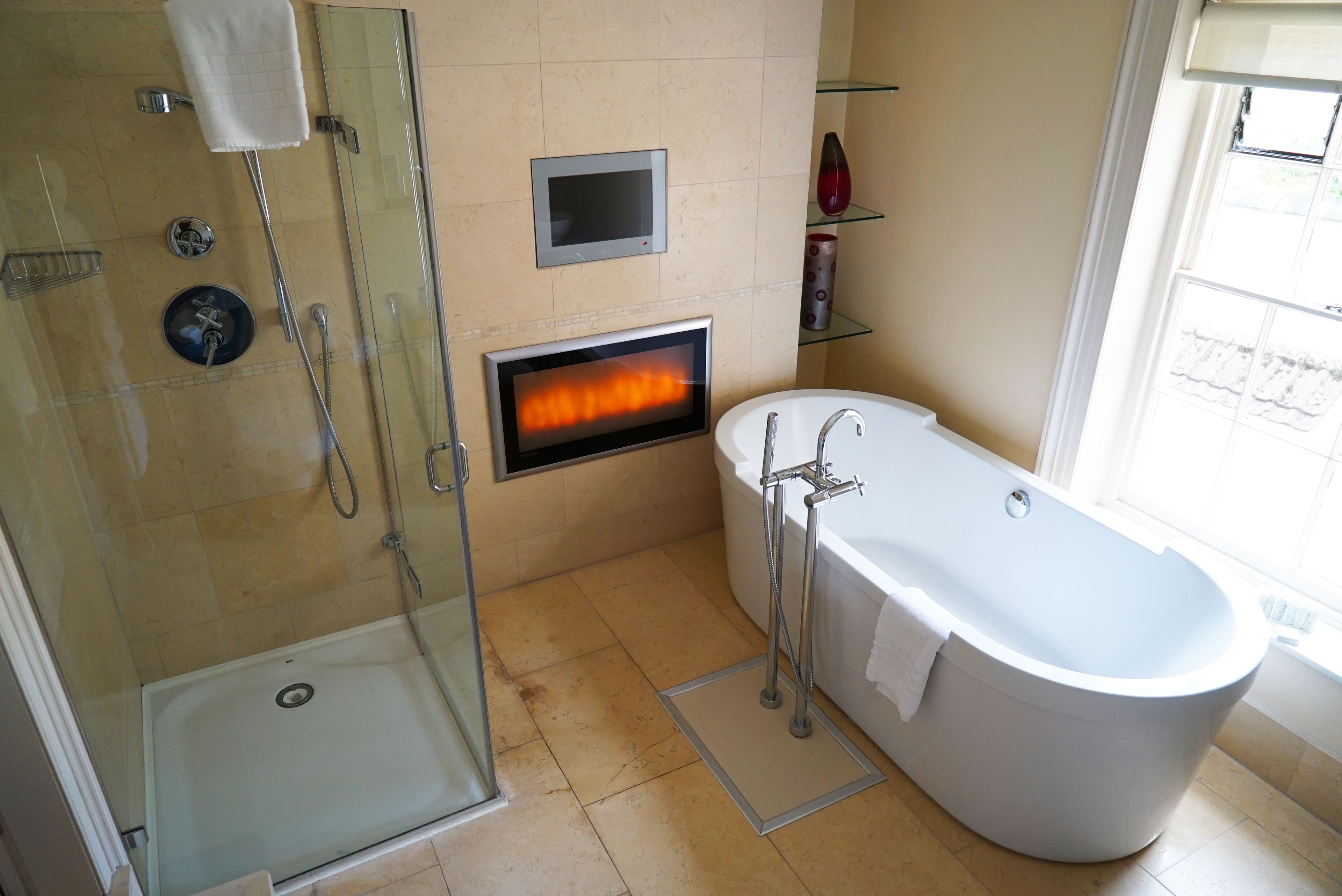 A modern bathroom with a glass-enclosed shower, a freestanding bathtub, and a built-in fireplace.
