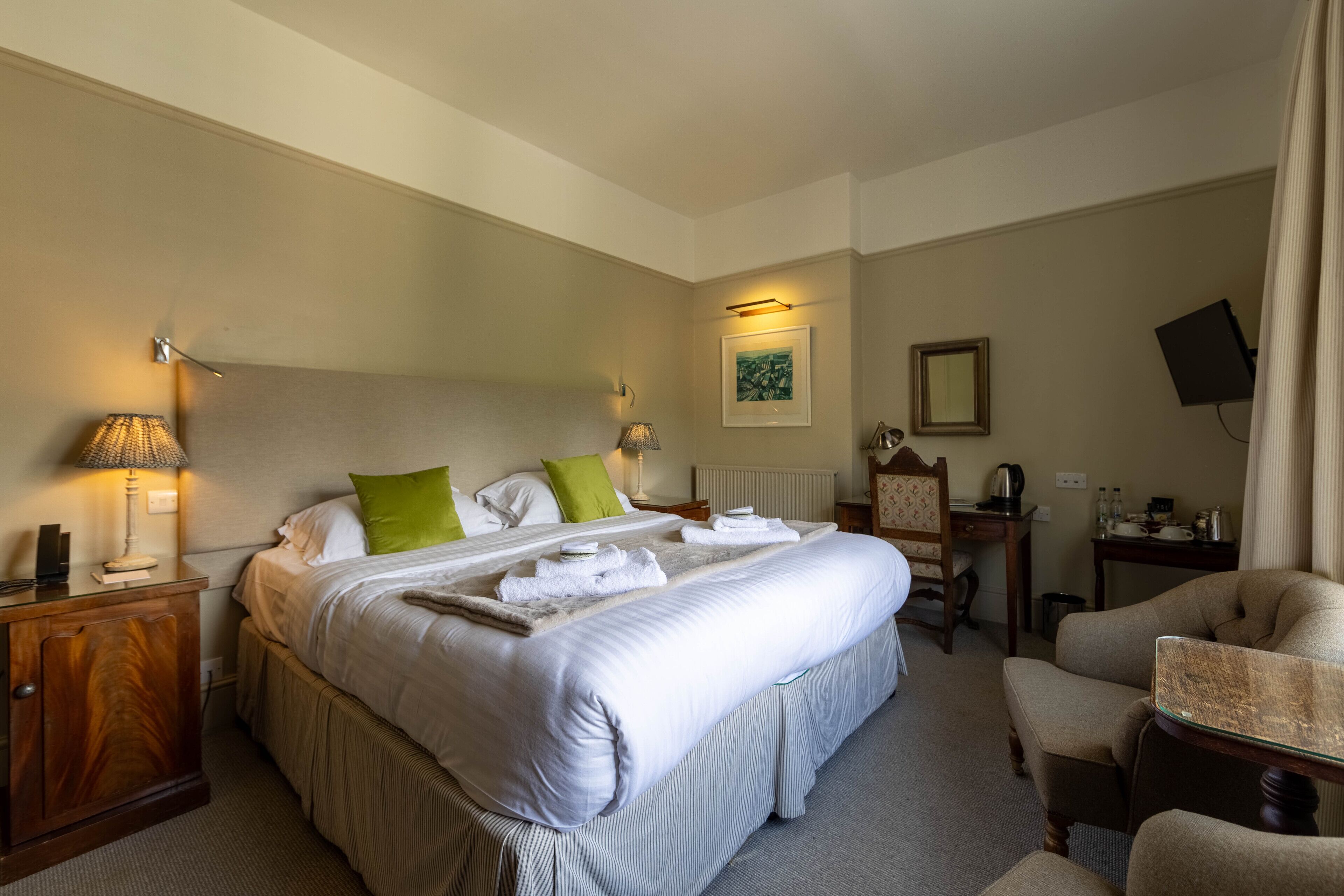 A hotel room with a large bed, bedside tables, a desk, a chair, and a television.