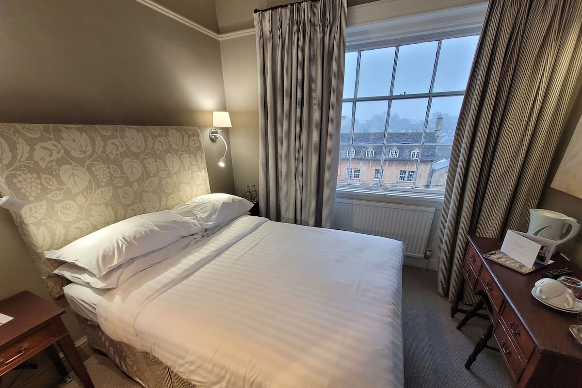 A hotel room with a bed, a nightstand, a lamp, a dresser, and a window with curtains.