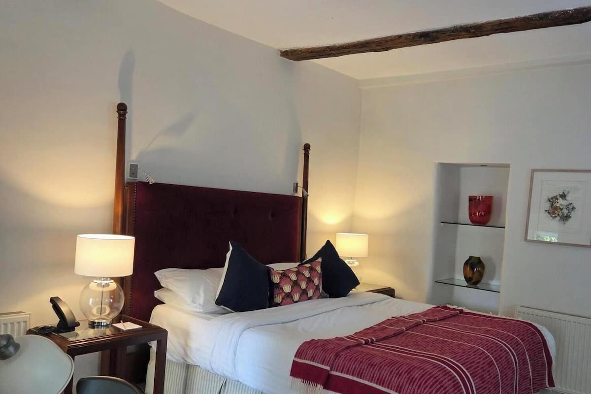 A hotel room with a bed, bedside lamps, a desk with a chair, and a small table.