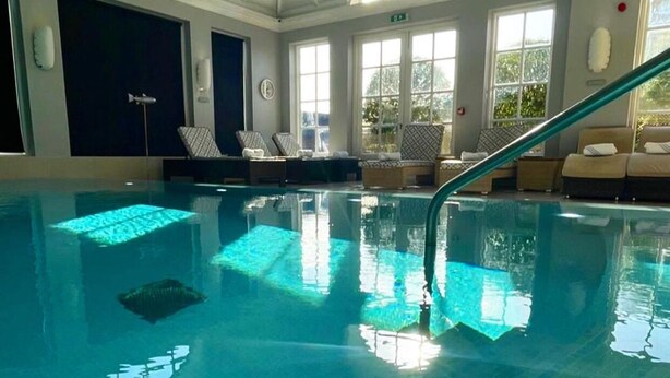 En indendørs swimmingpool med krystalklart blåt vand, et springbræt og solbeskinnelige vinduer.