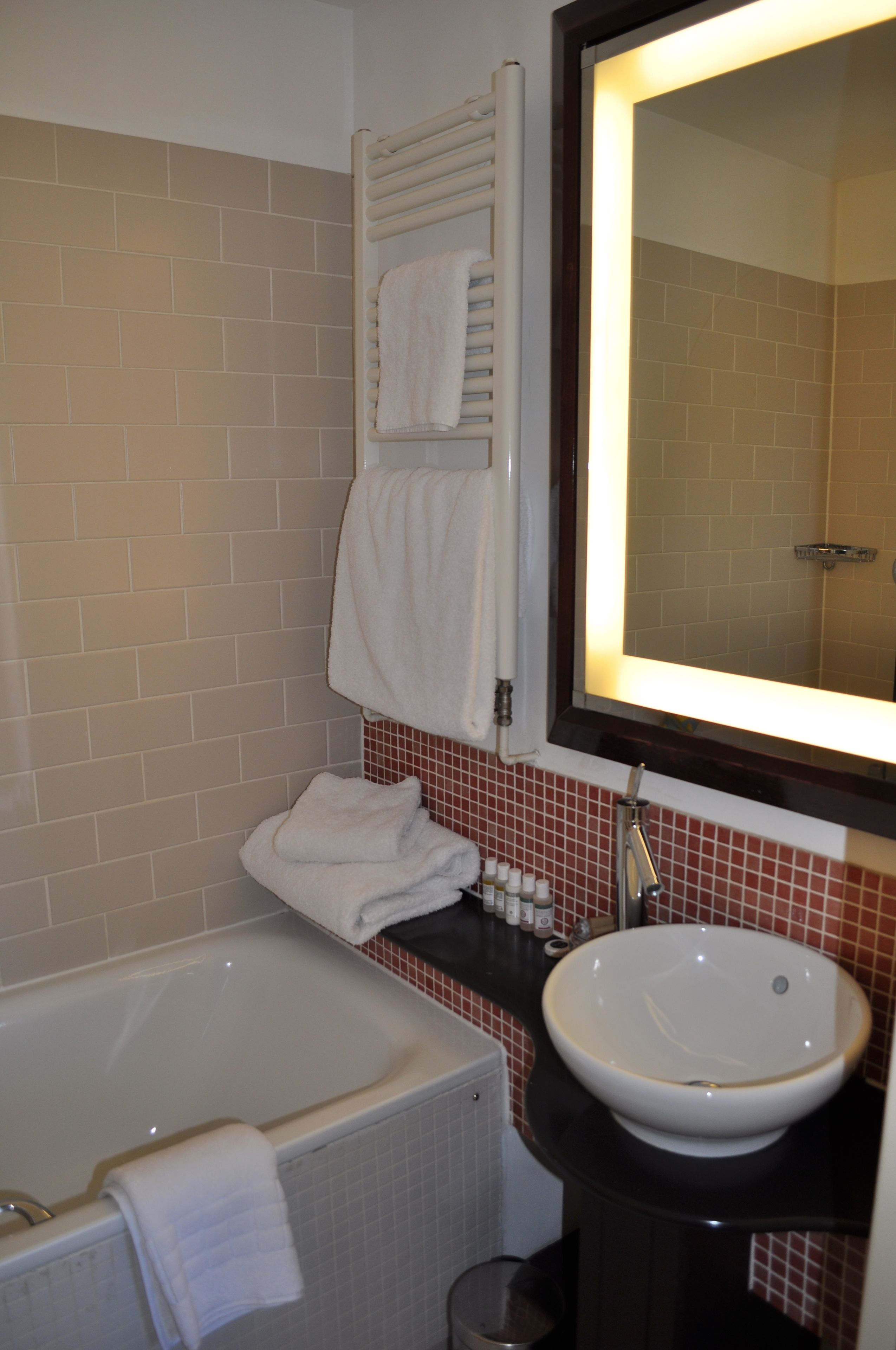 Un baño con bañera, lavamanos, espejo y toallero.