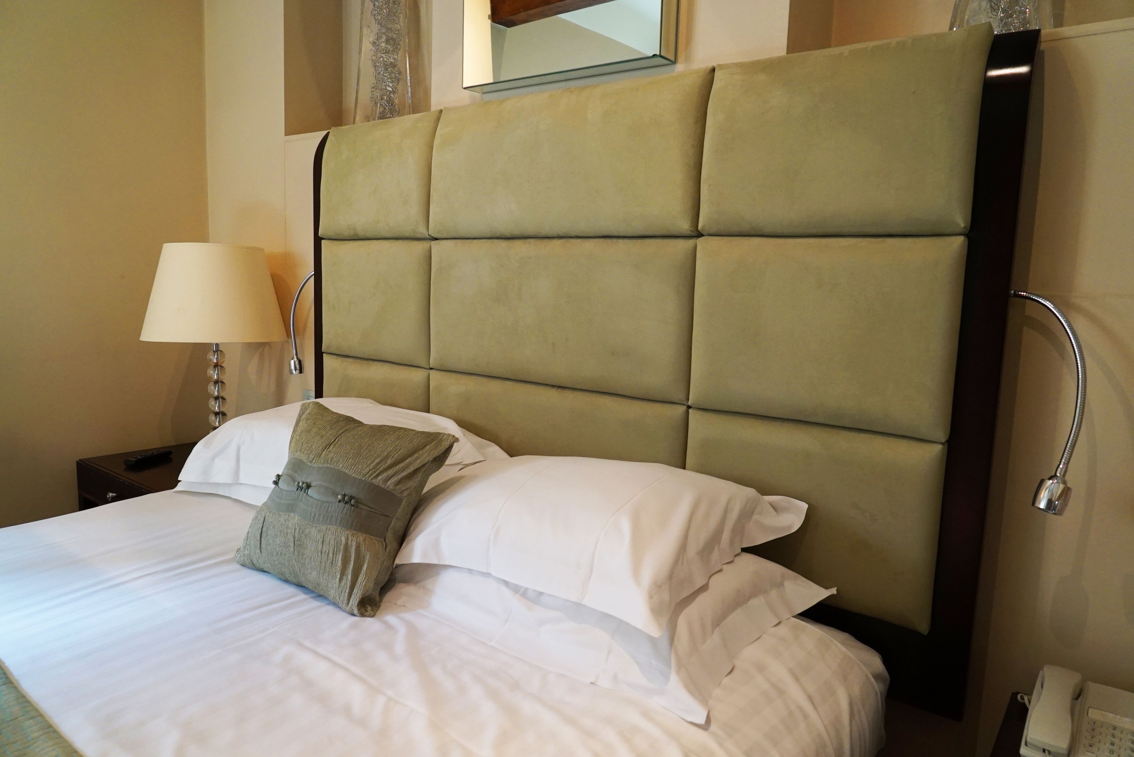 A neatly made bed with a tufted headboard, white linens, and a single decorative pillow.