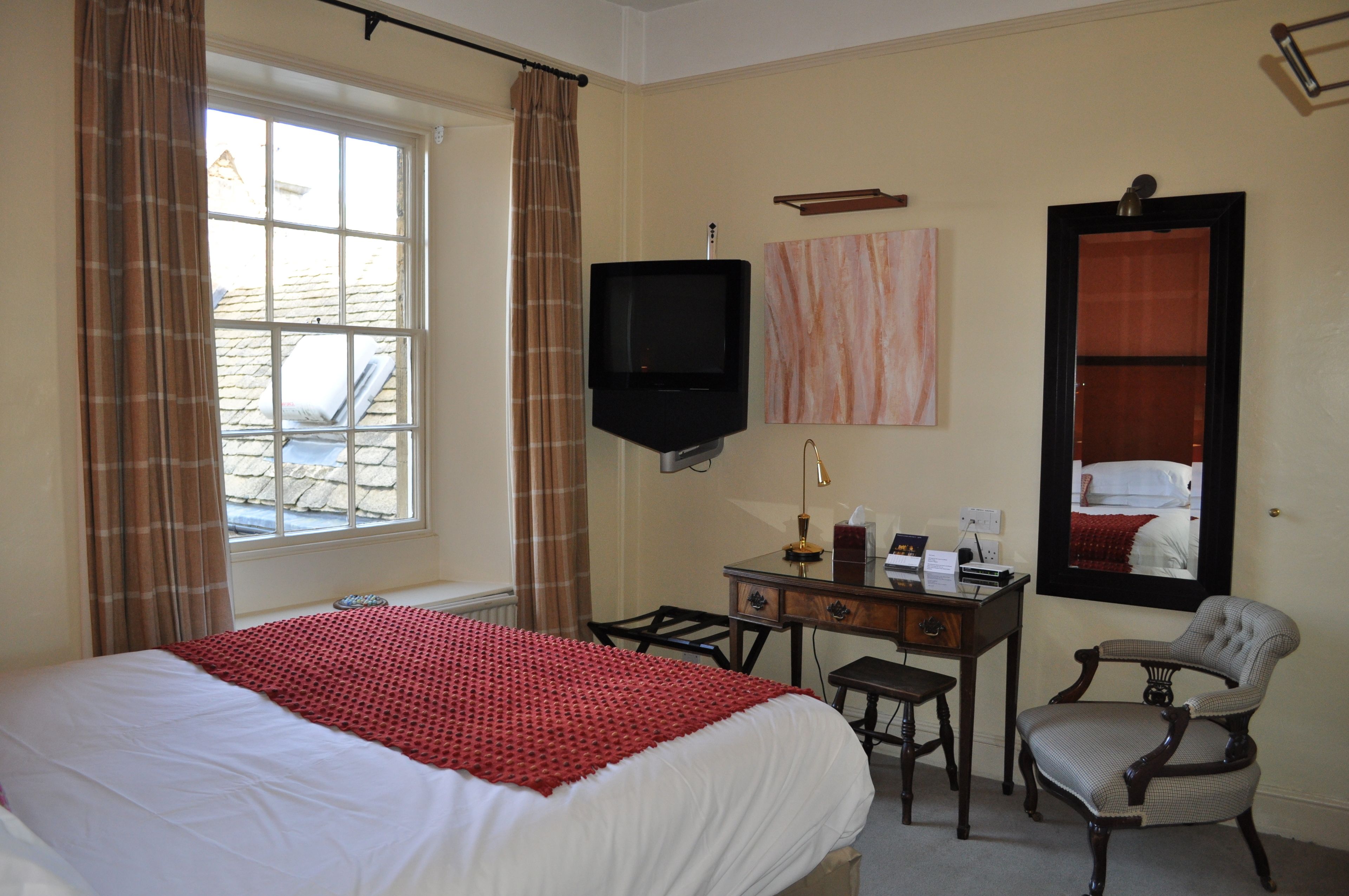 A hotel room with a bed, a desk, a chair, a television, and a window with curtains.