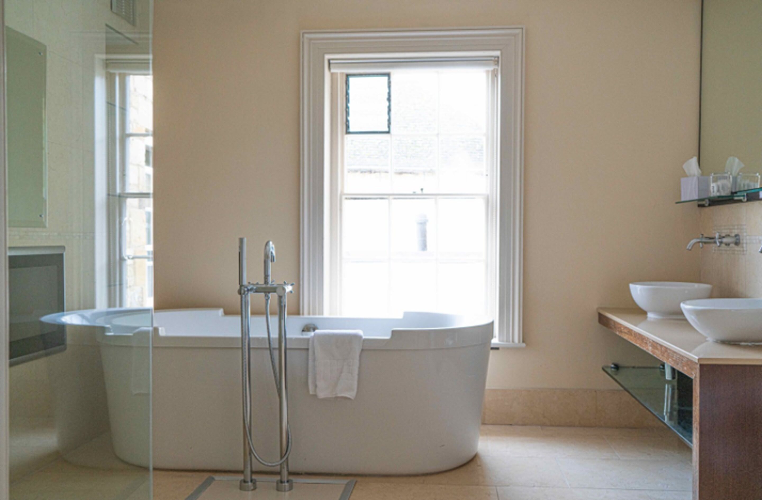A modern bathroom with a freestanding bathtub, a window, and a vanity with a sink and mirror.